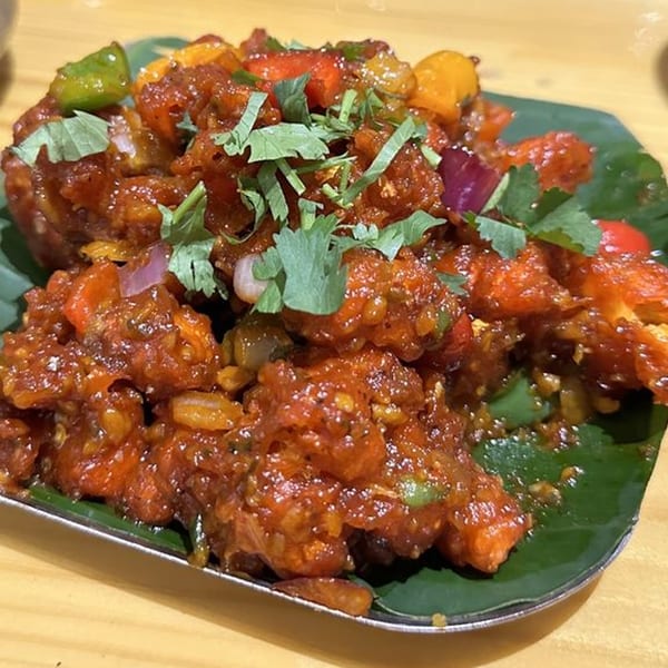 Kuppanna's spicy Indian chicken dish, garnished with fresh cilantro, bell peppers, and onions.