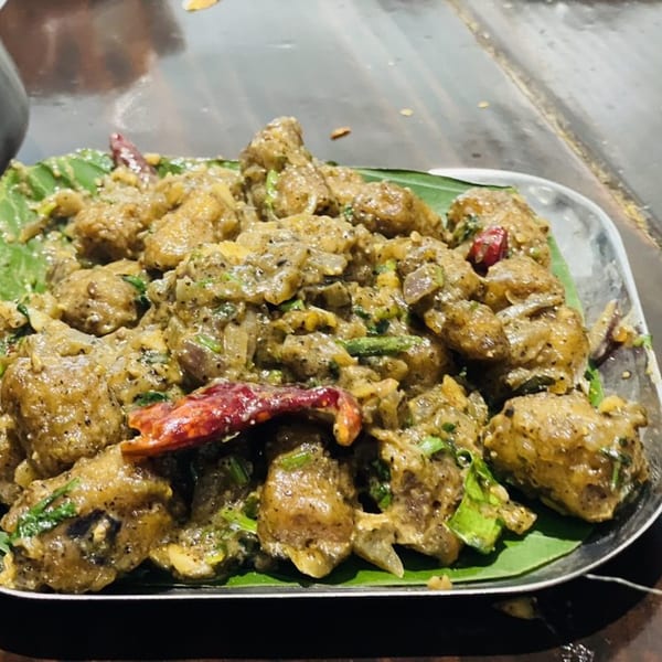 Kuppanna's South Indian chicken dish, garnished with red chilies and green herbs on a banana leaf.